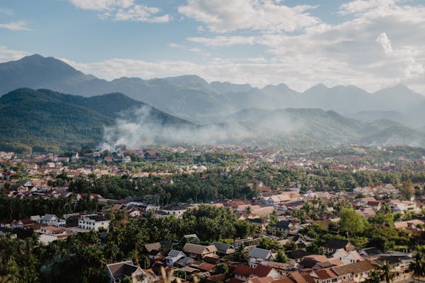 Drone view of picturesque valley with village located near mountain range against blue sky with fluffy clouds on sunny summer day